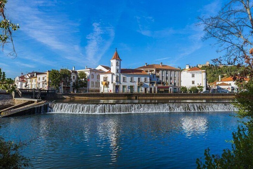 A river with a waterfall, buildings, and a tower. 1