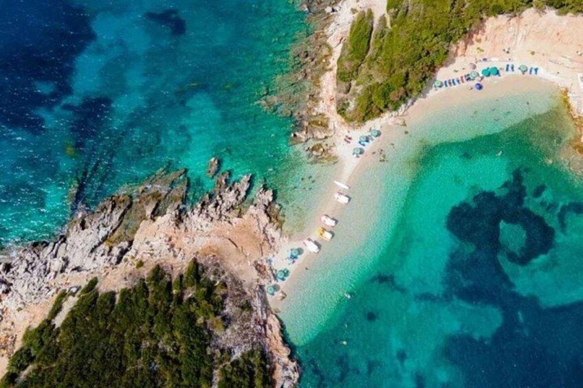 Luchtbeeld van een strand met helder turquoise water, een zandstrand en enkele parasols. 1