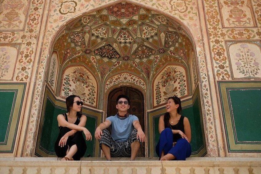 Three people sitting on steps in front of a building with intricate floral and geometric patterns. 2
