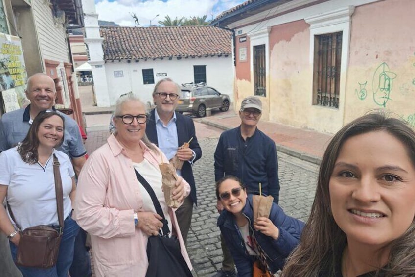 A group of people standing on a cobblestone street in a town with buildings that have colorful facades and some graffiti. 5