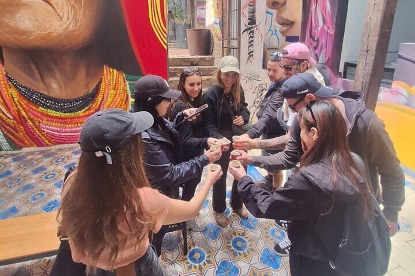 A group of people sitting in a circle, holding hands, with a mural and colorful tiles in the background. 3