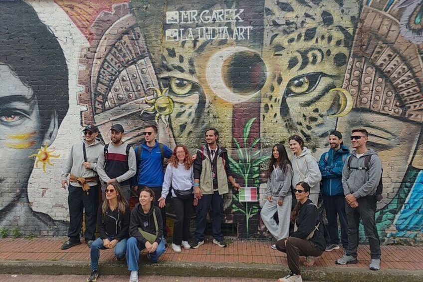 A group of people posing in front of a mural with a peacock and a woman's face. 2