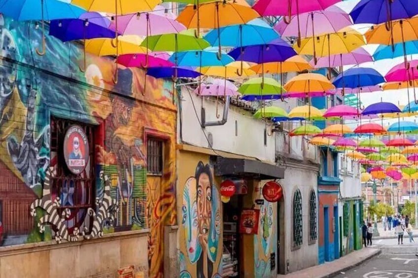 A street with colorful umbrellas hanging overhead and vibrant murals on the buildings. 4