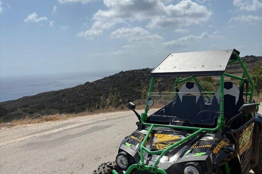 Un vehículo todoterreno verde estacionado en un camino de tierra con un paisaje costero al fondo. 4