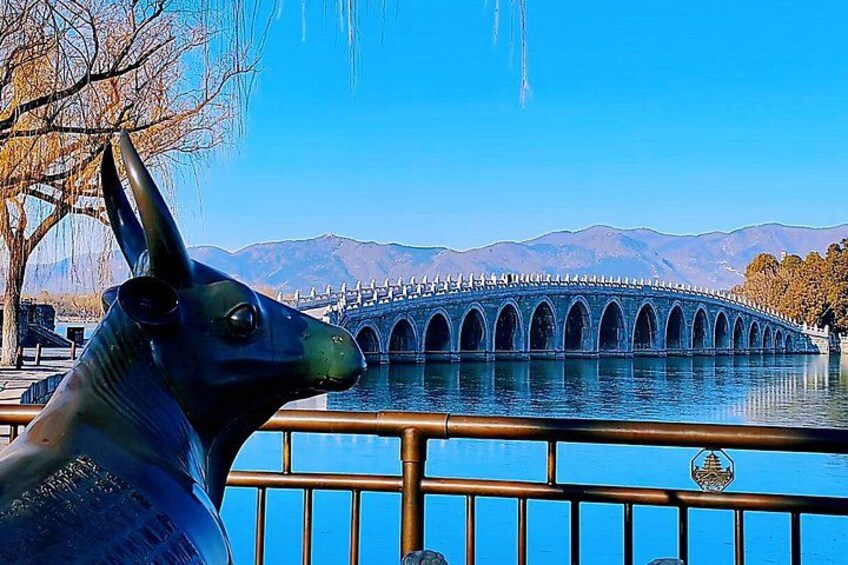 Una estatua de un perro, un puente y un cuerpo de agua con montañas al fondo. 1