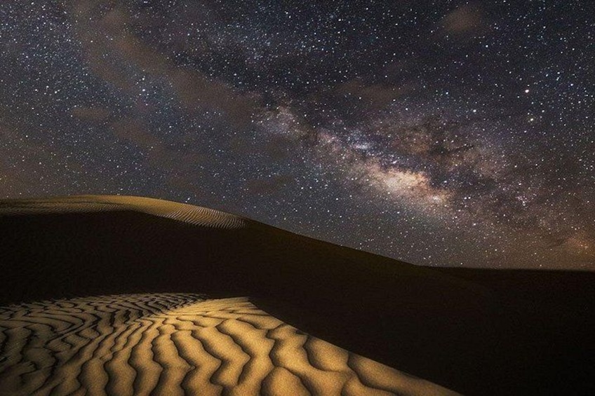 A starry night sky over a desert landscape with sand dunes. 3