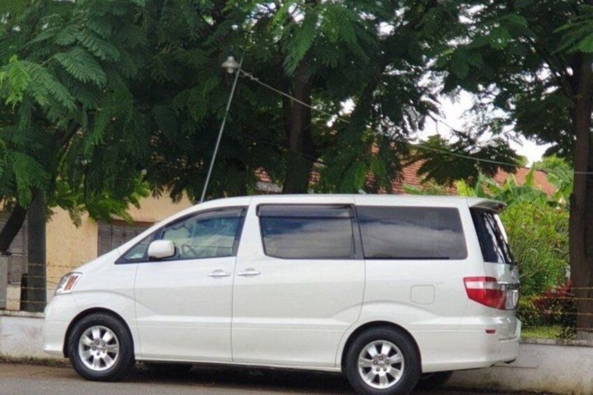 Una minivan blanca estacionada en una calle con árboles y un edificio al fondo. 4