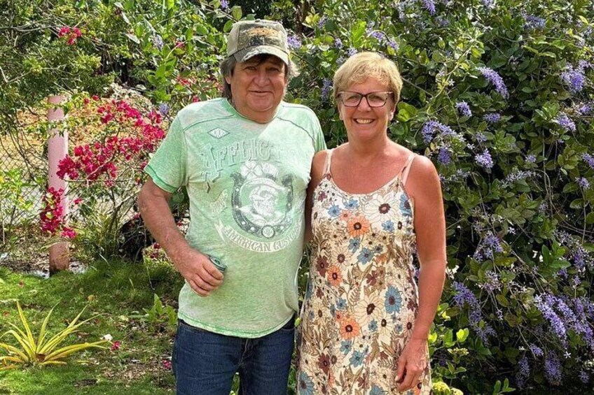 Two people standing in a garden with flowering plants and a fence. 4
