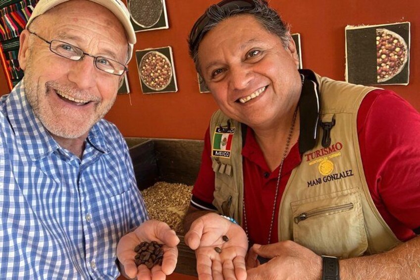 Two individuals holding coffee beans, with a coffee grinder and a wall displaying coffee-related items in the background. 4