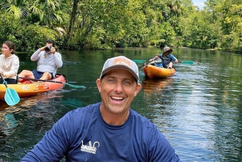 A man kayaking on a river surrounded by lush greenery. 1