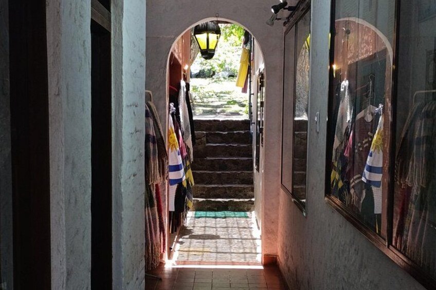 A narrow passageway with a staircase leading to a garden, flanked by walls with clothing displays. 5