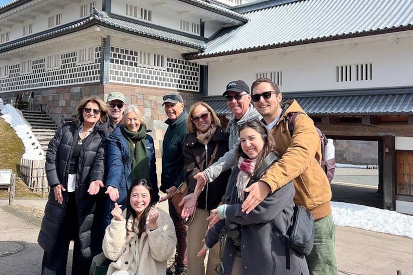A group of people posing in front of a traditional building with a tiled roof and stone walls. 3