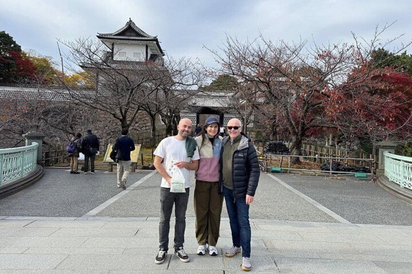 A group of people standing in front of a traditional Japanese building with a pagoda, surrounded by cherry blossom trees. 4