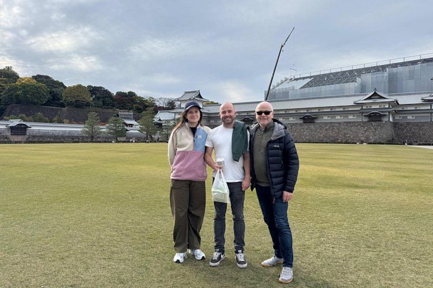 Three people standing on a grassy field with a traditional Japanese building in the background. 2