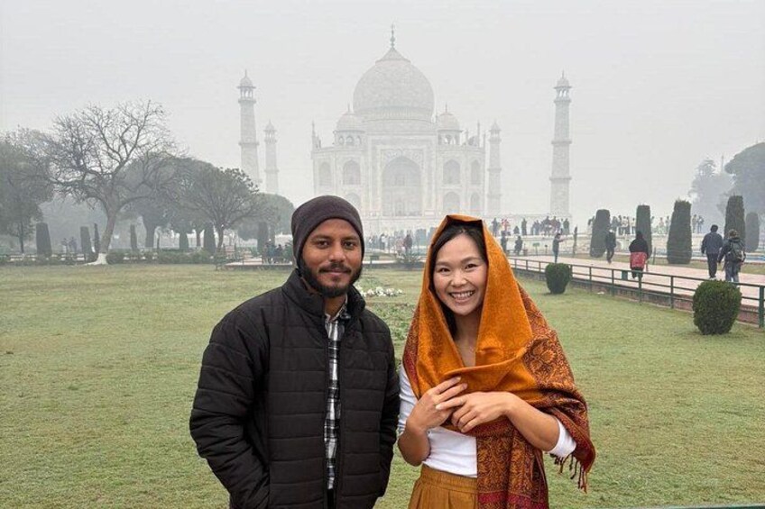 Two people standing in front of the Taj Mahal with a foggy background. 2