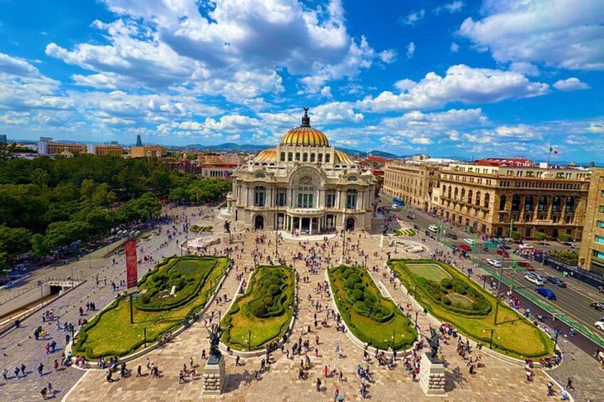 Una amplia plaza pública con un edificio destacado que presenta una cúpula dorada, rodeada de jardines cuidados y calles concurridas. 1