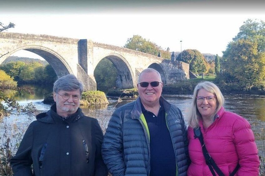 Three people standing in front of a stone bridge over a river. 4