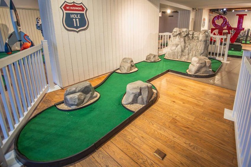 A miniature golf course with a green carpet, wooden floor, and rock obstacles. 3