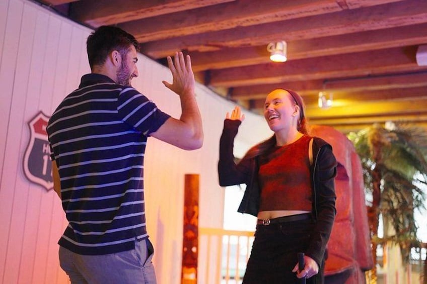 Two people engaging in a high-five in an indoor setting with wooden beams and a wall with a shield emblem. 2