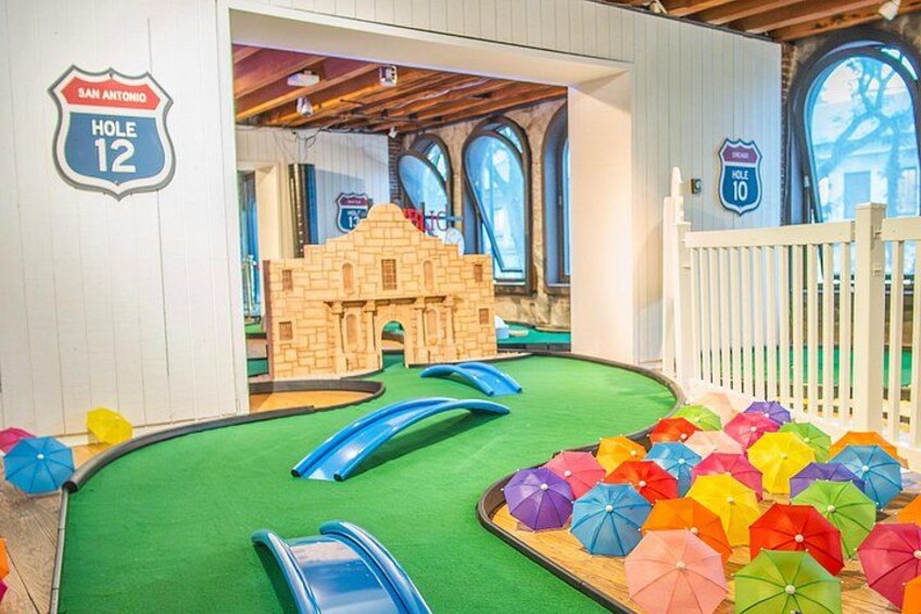A miniature golf course with a sandbox castle, slides, and colorful umbrellas. 4