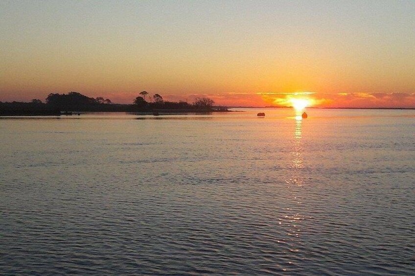 A sunset over a calm body of water with a distant shoreline and a few boats. 2