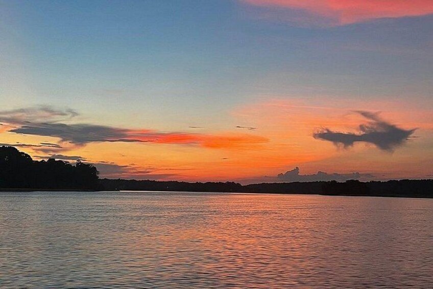 Solnedgang over et roligt vandareal med silhuetter af træer i horisonten. 2