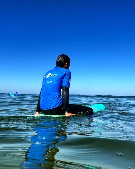 A person sitting on a surfboard in the ocean, wearing a blue shirt and black shorts. 4