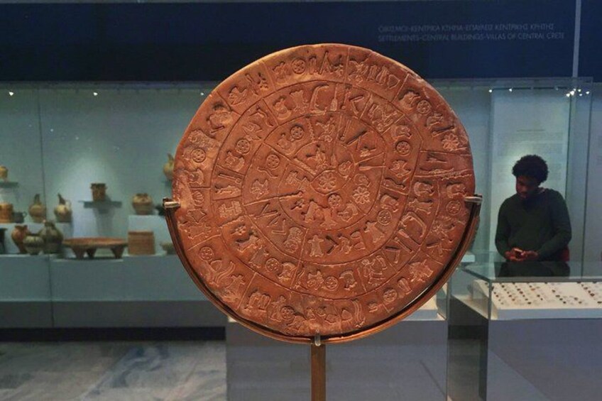 A circular artifact with intricate carvings, displayed in a museum setting with glass cases and other exhibits in the background. 4