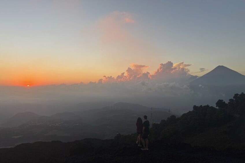Un coucher de soleil avec une montagne en arrière-plan et deux personnes debout sur une colline. 2