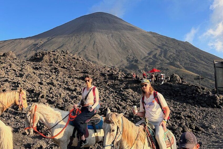 Des personnes à cheval traversent un terrain rocheux, avec un volcan en arrière-plan. 5