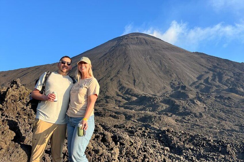 Deux personnes se tiennent devant une montagne volcanique, sous un ciel dégagé. 3