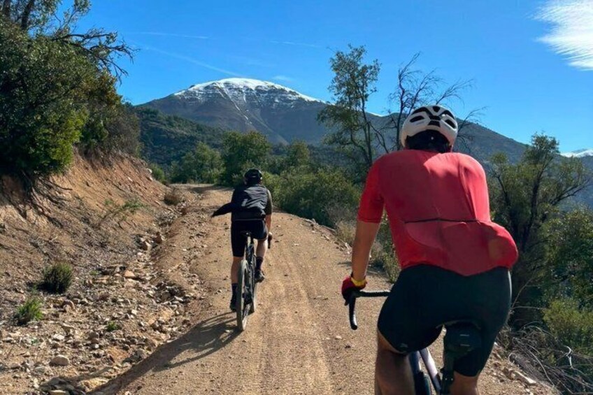 Two cyclists on a dirt path with a mountain in the background. 3