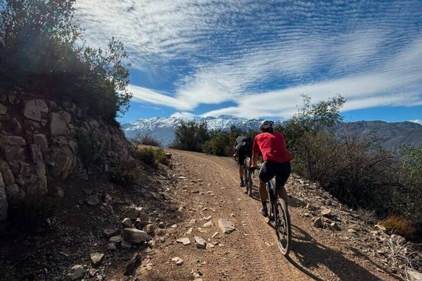 Two cyclists on a rocky trail with a mountain range in the background. 4