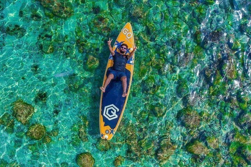 A person on a surfboard in clear turquoise water with visible marine life and coral formations. 2