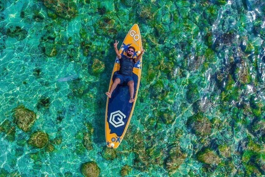 A person lying on a surfboard in clear turquoise water with visible marine life. 2