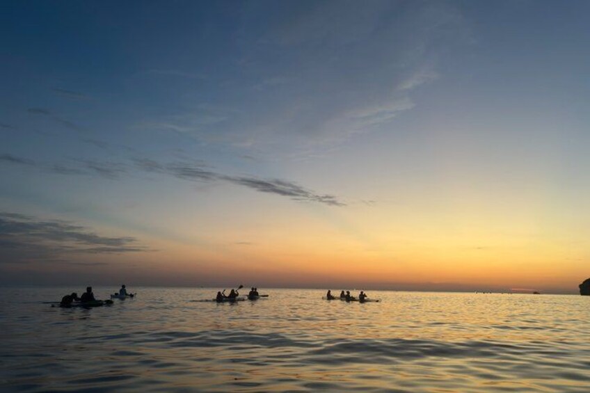 A sunset over a calm sea with several boats and people on the water. 3