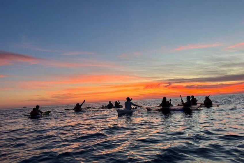 A group of people in canoes on a body of water during sunset. 1