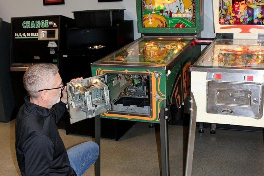 Un hombre observando una máquina de pinball antigua con ranura para monedas y una exhibición colorida. 3