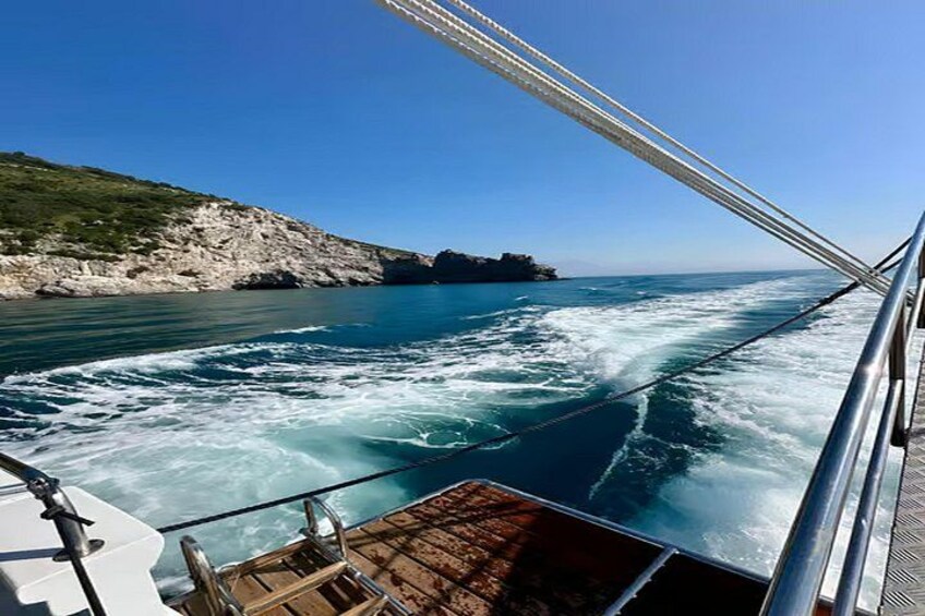 A boat on a body of water with waves, a rocky coastline, and a clear sky. 1