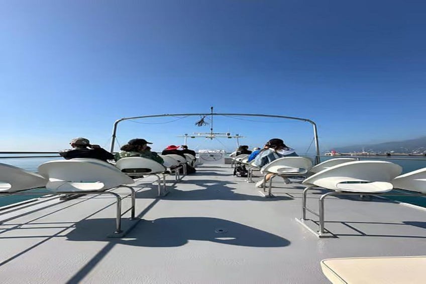 Cubierta de barco con gente sentada en mesas, cielo despejado y una costa lejana. 4