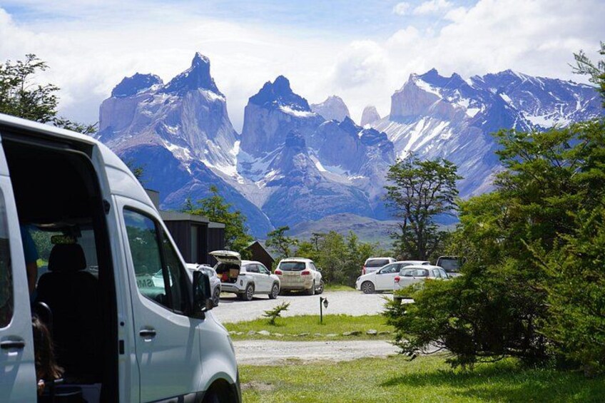 A parking area with vehicles, a van, and a mountainous landscape in the background. 1