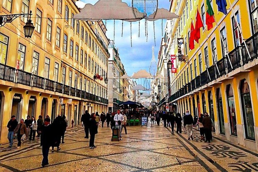 A bustling street with yellow buildings, people walking, and a patterned pavement. 3