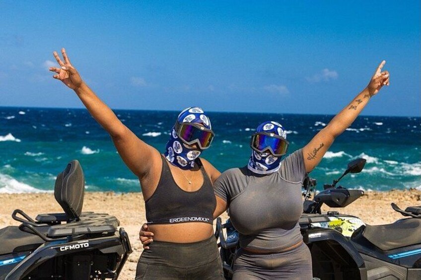 Deux personnes portant des casques, debout sur une plage, avec une moto et l’océan en arrière-plan. 4