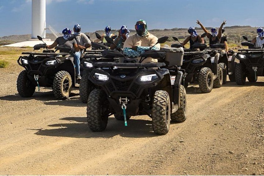 Un groupe de personnes circulant en quads sur un chemin de terre, avec un moulin à vent en arrière-plan. 3
