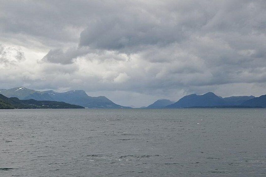 A body of water with mountains in the background under cloudy skies. 1