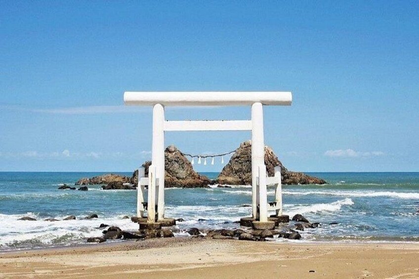 A white wooden structure on a beach with waves crashing against rocks in the background. 4