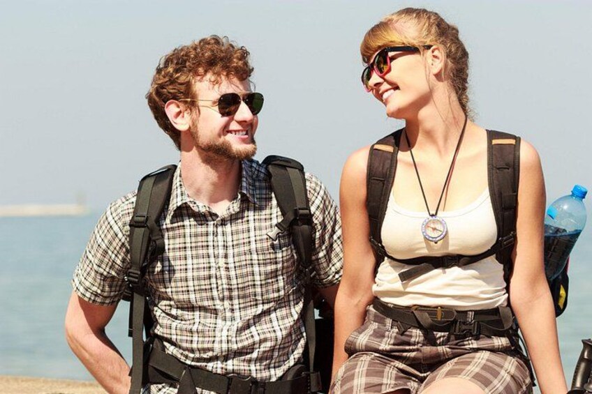 Two people sitting by the seaside, one with a backpack and the other with a water bottle. 1