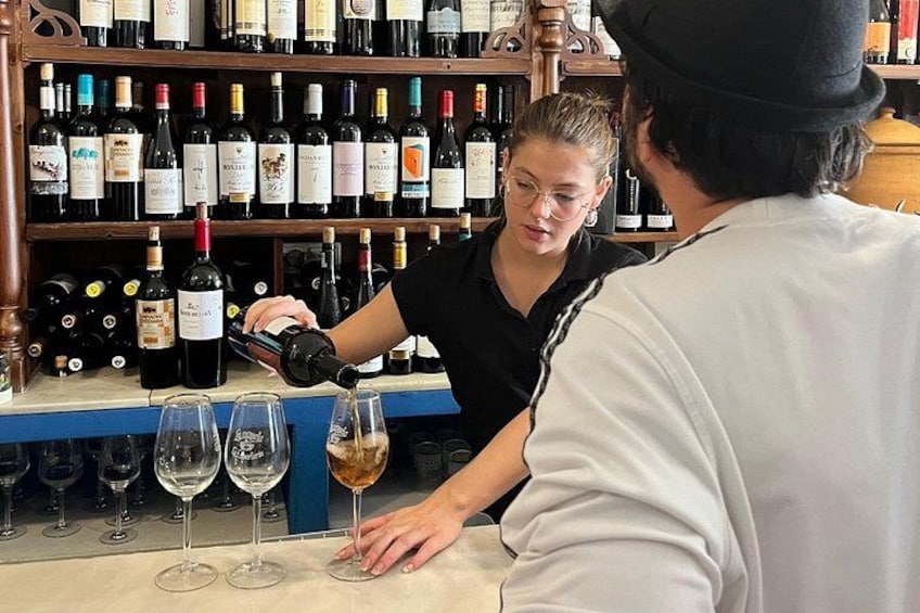 A person pouring wine into a glass at a bar with a wine rack in the background. 5