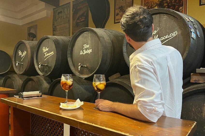 A person at a bar with wine glasses and a menu. There are wooden barrels in the background. 1