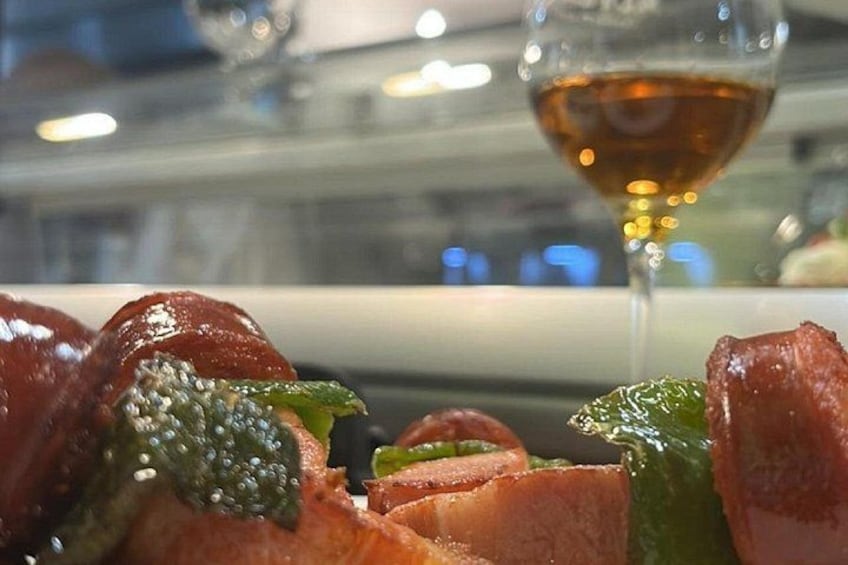 A dish of sliced meat with a green vegetable, possibly asparagus, and a glass of red wine in the background. 3